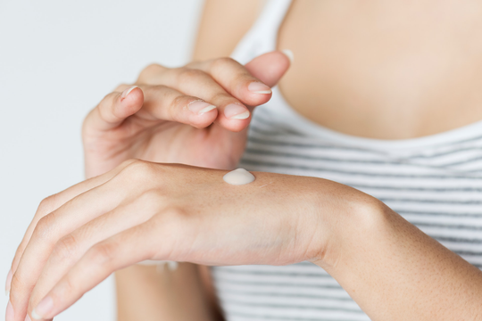 A woman puts a small drop of lotion on the back of her hand, using Eco Chic Movement non toxic skincare products