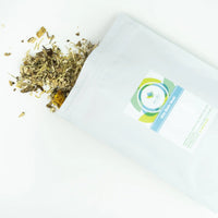 A pouch of sitz bath for postpartum healing lays on a white table with some of the herbs spilling out