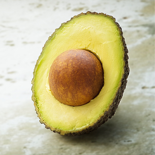 An avocado is shown on a tan background - one of the all natural skincare ingredients in Eco Chic Movement's products
